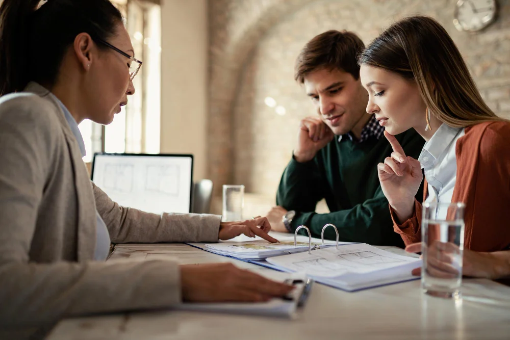 young-man-his-wife-examining-housing-plans-with-real-estate-agent-meeting-office